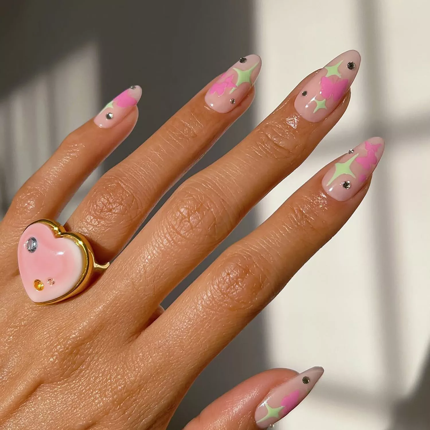 a strawberry milk mani topped with green stars and bubblegum pink butterflies