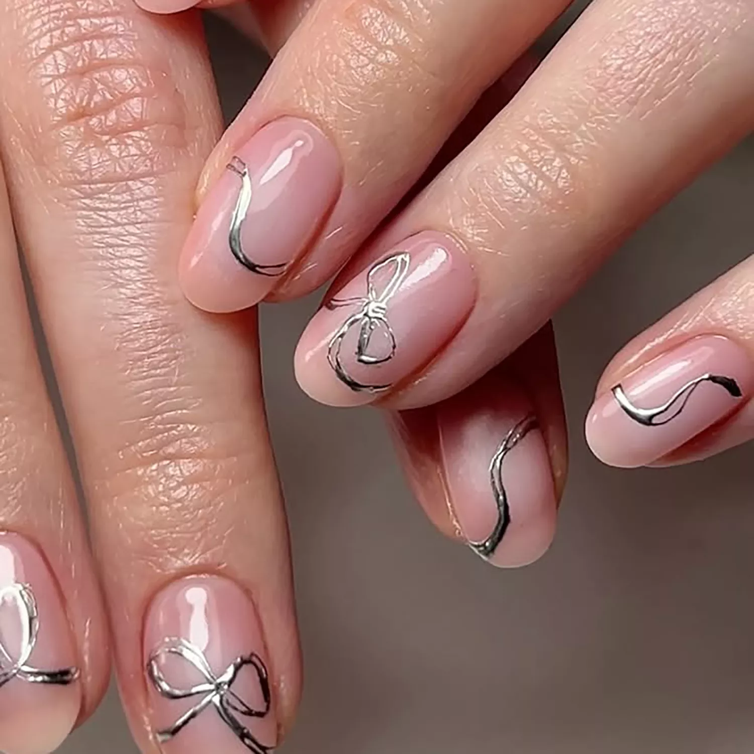 a strawberry milk manicure topped with chrome silver bows