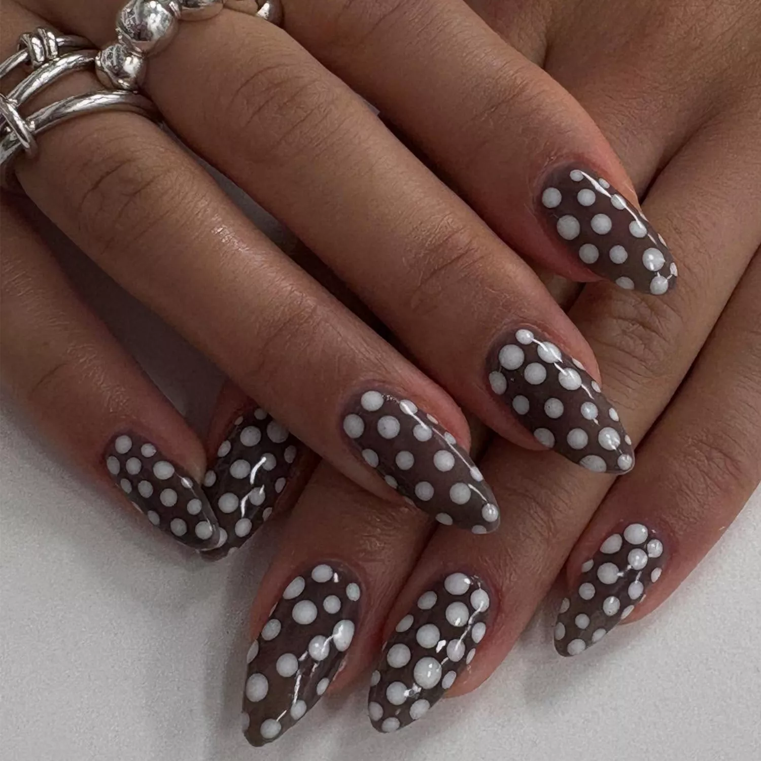 Two hands folded over each other with brown base polish and white polka dots