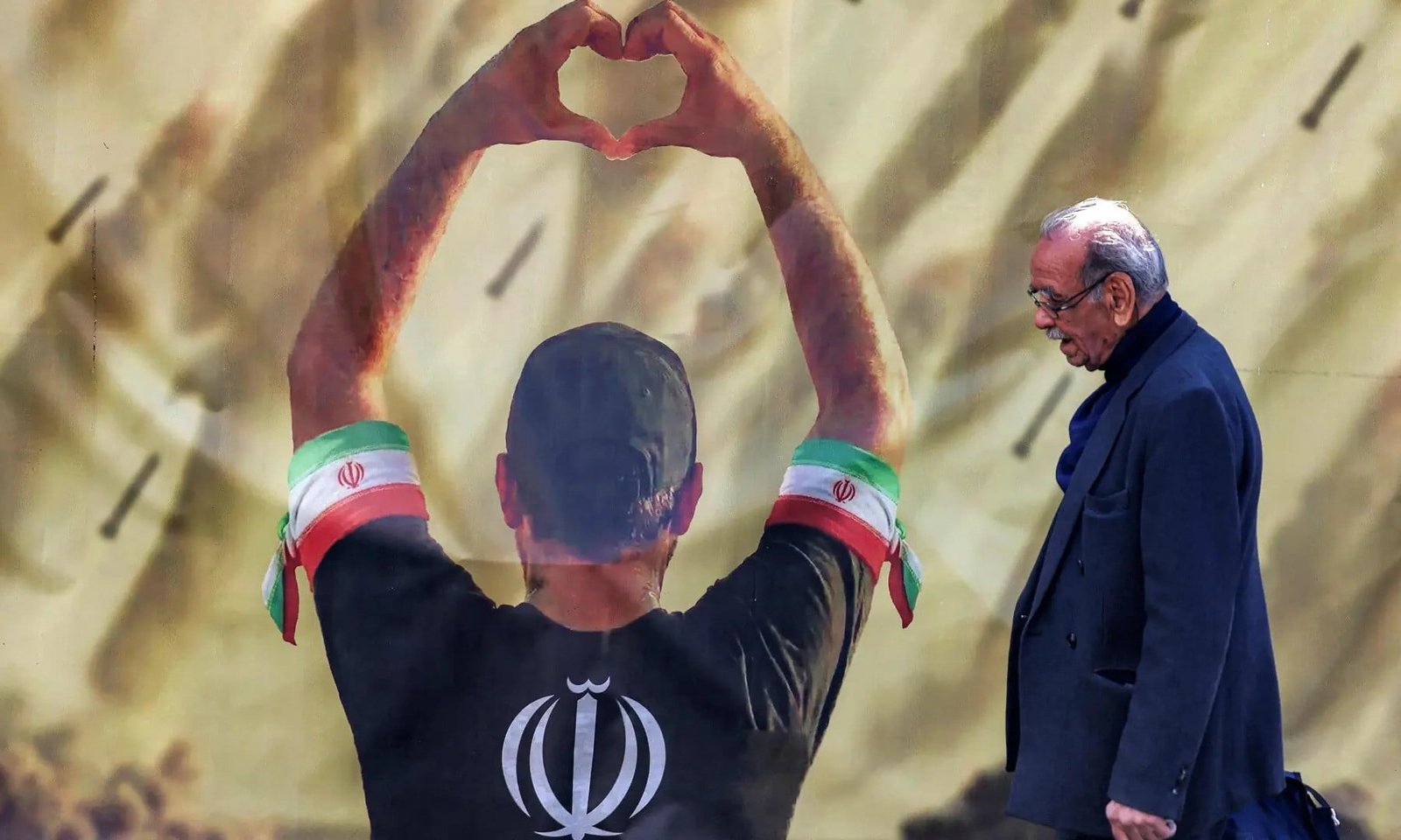 This photo taken on April 6, 2026 shows a man walking past a banner depicting a man holding up a heart gestures before missiles being fired, in Tehran. — AFP/File